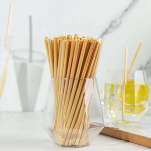 Bamboo straws in a clear glass container on a marble countertop.