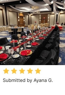 Table setting in a banquet hall with black tablelcoth and chair covers, charger plates, red napkins, and ceiling drapes by Ayana G