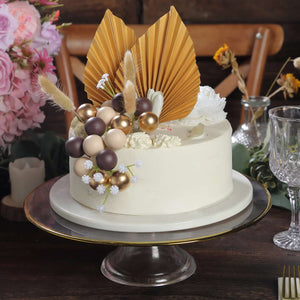 Elegant cake with decorative leaves and chocolate spheres on a glass stand.