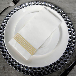 Elegant white napkin with gold Greek key design on a decorative plate.