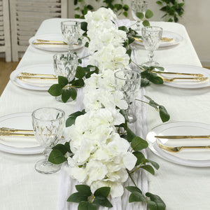 Elegant white floral table runner with glassware and cutlery on a dining table.