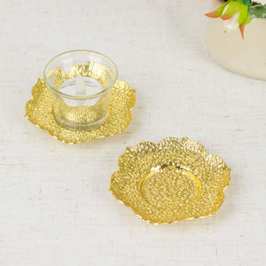 Gold decorative plates with a glass candle holder on a textured surface.