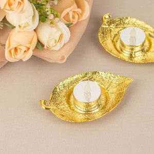 Gold leaf-shaped candle holders with tea lights beside soft pink roses.