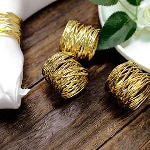 Gold wire napkin rings on a wooden table with a white plate and napkin.