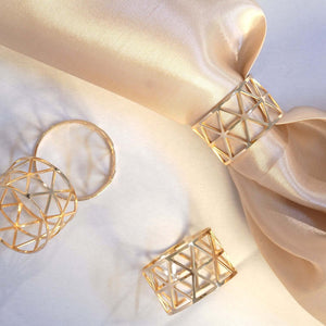 Gold geometric napkin rings elegantly displayed on a soft fabric backdrop.