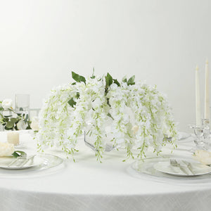 White floral centerpiece with cascading orchids on a dining table.