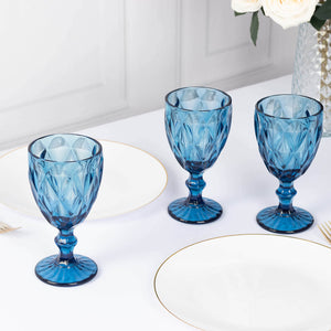 Set of three blue glass goblets on a table with white plates and floral decor.