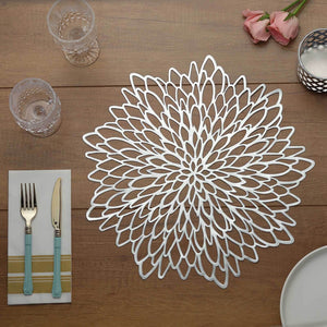 Elegant silver floral placemat on wooden table with cutlery and glasses.