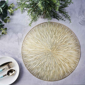 Gold textured round placemat on a gray surface with greenery and tableware.