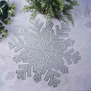 Gray snowflake placemat on a textured surface with greenery