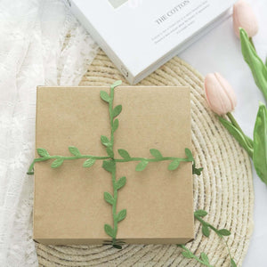 Gift box wrapped in green vines on a textured surface with flowers.