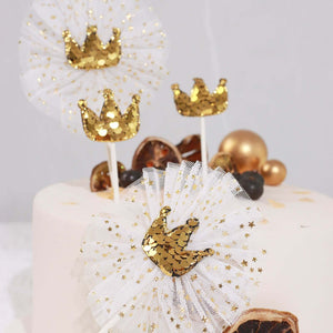 Gold crown cake toppers with tulle accents on a decorated cake.