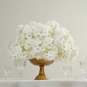 White floral arrangement in a gold vase with crystal glasses.