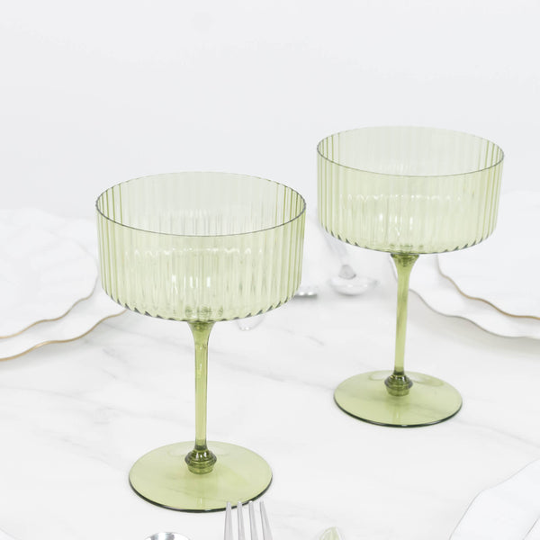 Two green ribbed coupe glasses on a white marble table.
