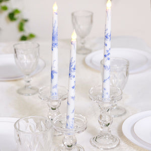 Blue floral candles in glass holders on a dining table setting.