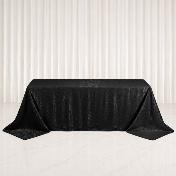 Black jacquard rectangular tablecloth draped over banquet table on white backdrop