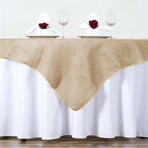 Burlap table runner with gold trim on a white tablecloth, set for dinner.