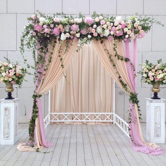 Elegant wedding arch with floral arrangements and draped fabric in soft pink and cream.