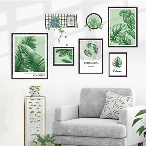Framed tropical leaf art prints arranged on a wall above a gray sofa with plants.