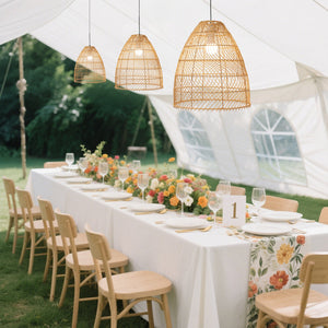 Outdoor wedding reception with a long table, floral centerpiece, and hanging pendant lights.