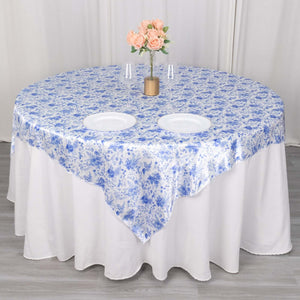 Blue floral tablecloth on a round table with plates and flowers.