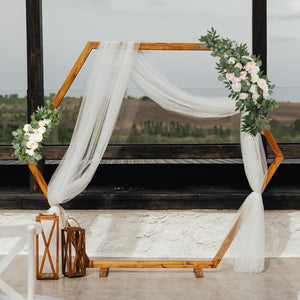 Wooden hexagon frame with draped fabric and floral decor, set in a scenic venue.