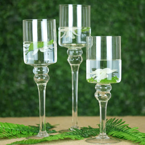 Elegant glass candle holders with flowers and water, set against a green backdrop.
