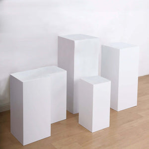 Set of four white display pedestals in various heights on a light wooden floor.