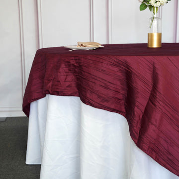 Create a Luxurious Atmosphere with a Burgundy Accordion Crinkle Taffeta Square Table Overlay