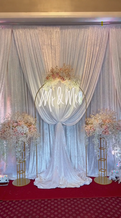 Wedding backdrop setup with curtains, backdrop stands, artificial flowers, and neon light