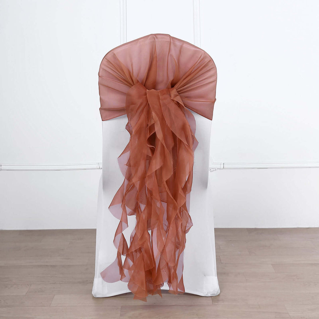 Brown chiffon chair sash tied on a white chair against a plain background.