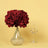 Red flower bouquet in crystal vase with wine glass on yellow background.