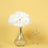 White hydrangea flowers in a clear glass vase with a wine glass on a yellow background.