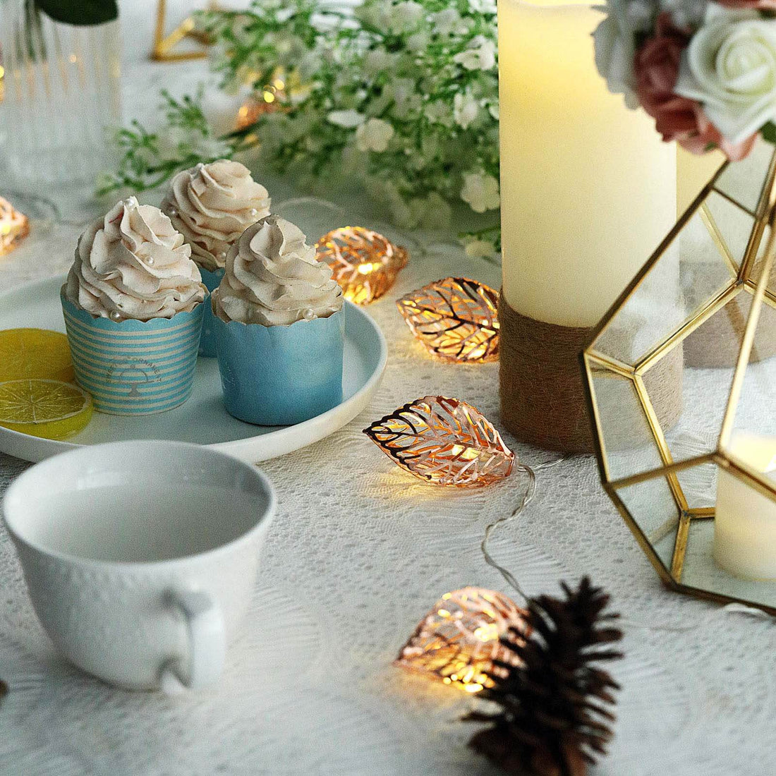 Decorative dessert setup with cupcakes, candles, and fairy lights on a table.