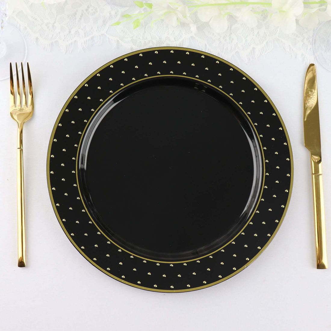 Black decorative plate with gold accents and cutlery on a white tablecloth.