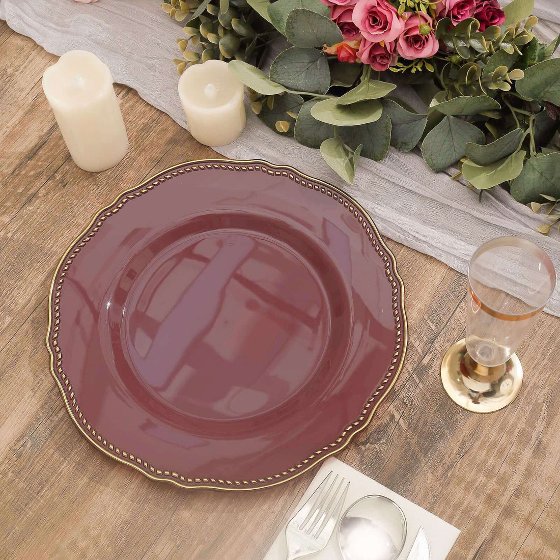 Elegant burgundy plate with gold trim on a rustic wooden table setting.