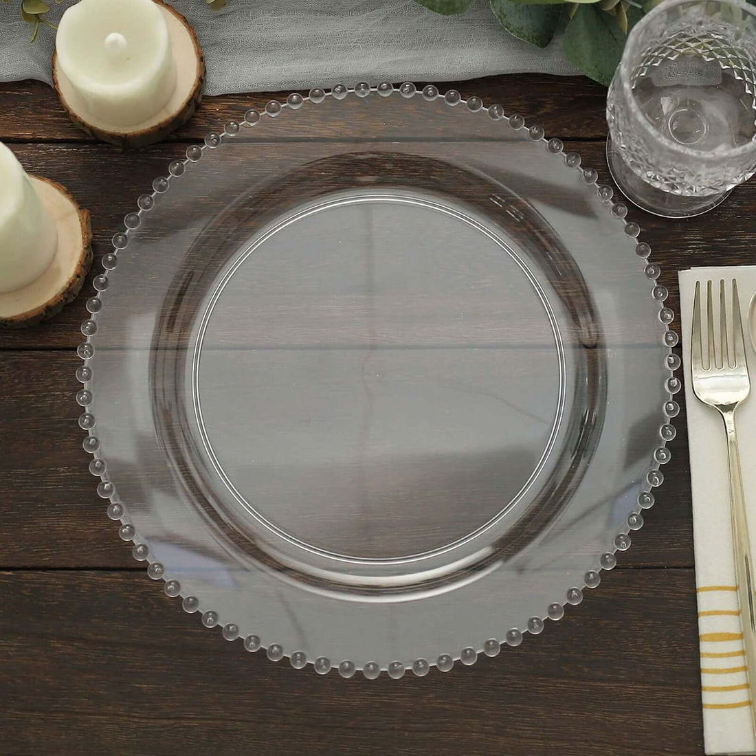 Clear glass charger plate with beaded edges on a wooden table.