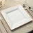 Square white dinner plate with rose gold trim on a dining table setting.
