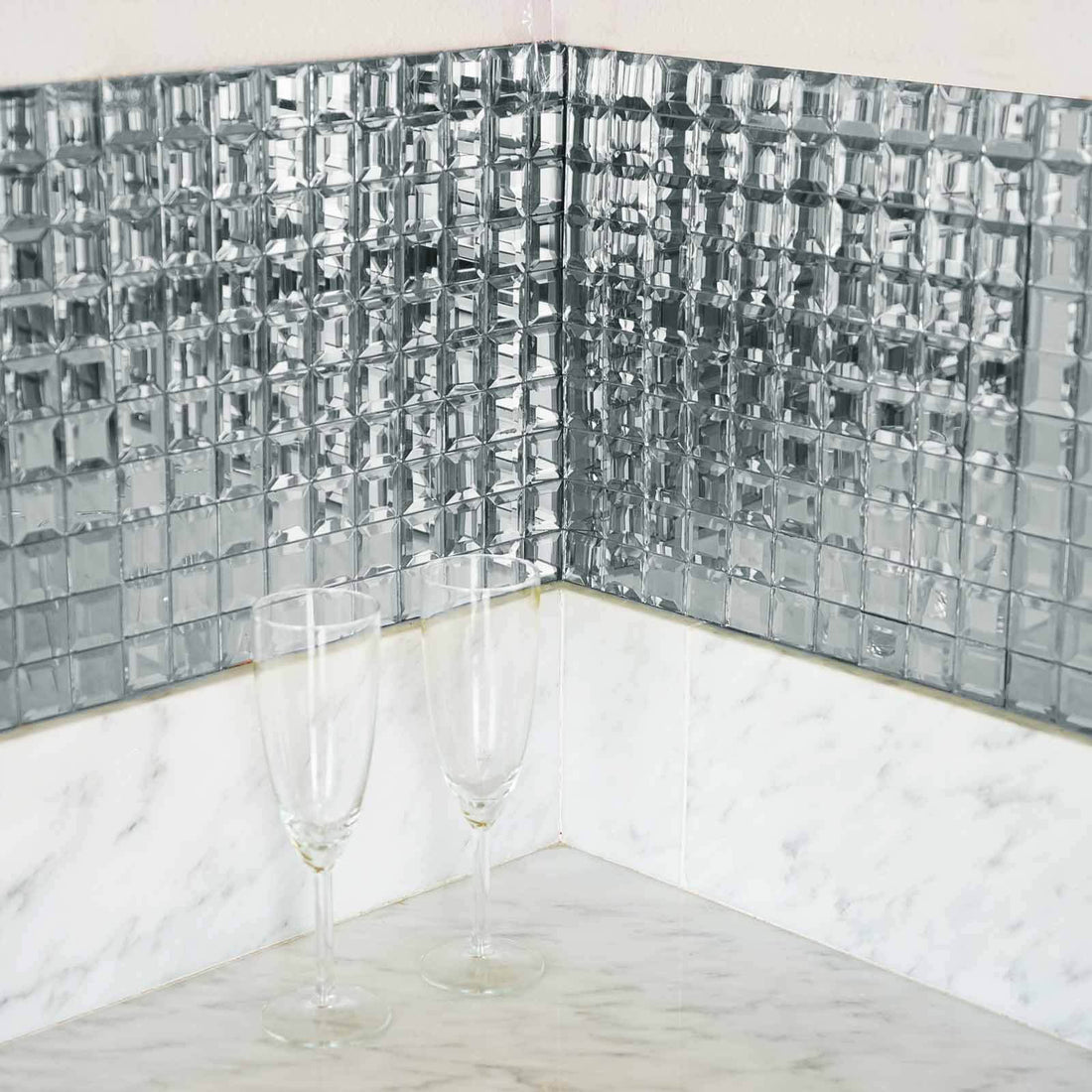 Mirrored tile backsplash in corner with champagne flutes on marble countertop.