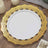 Elegant white plate with intricate gold lace design on a wooden table.