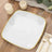 White square plate with gold rim on wooden table with candles and cutlery.