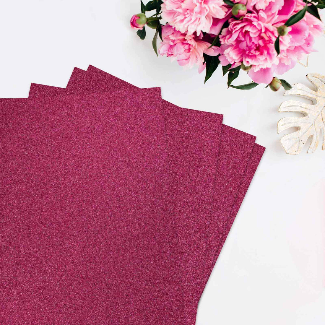 Sparkly magenta craft paper sheets stacked with flowers in the background.