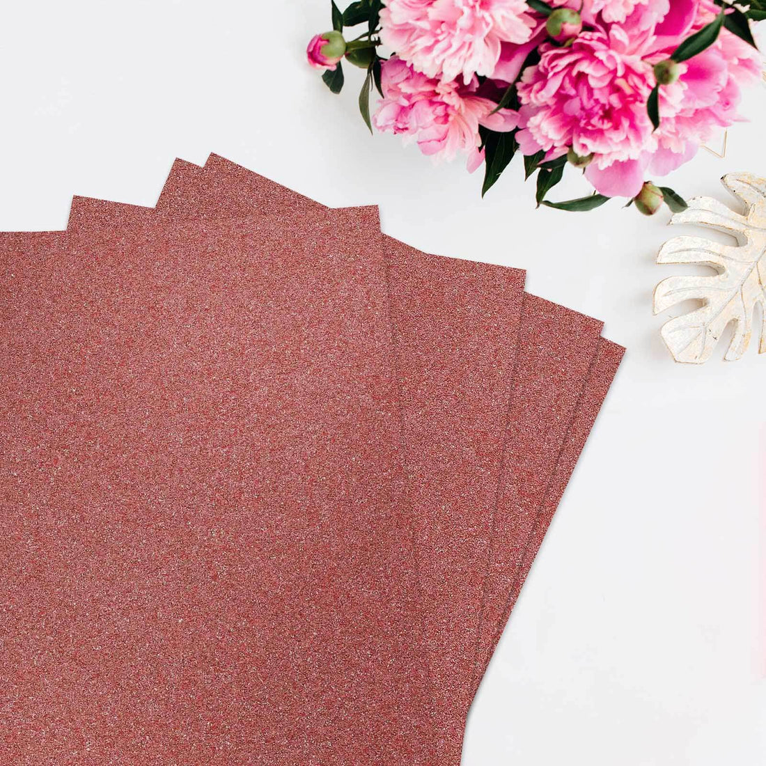 Glitter cardstock sheets in rose gold with pink flowers in the background.