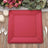 Red square charger plate on a wooden table with floral decor and cutlery.