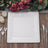 Elegant square white dinner plate with floral design, set on rustic wooden table.