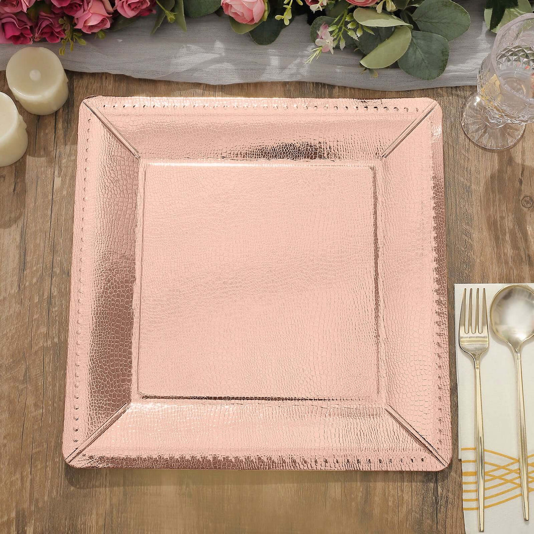Rose gold square charger plate on a rustic wooden table with floral decor.
