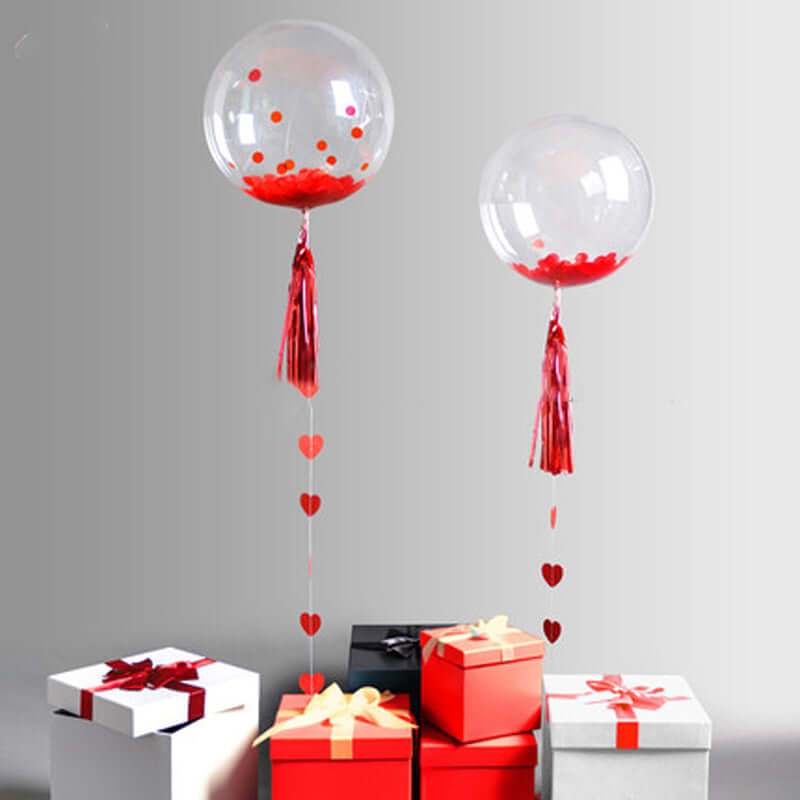 Clear balloons with red confetti and heart accents above gift boxes.