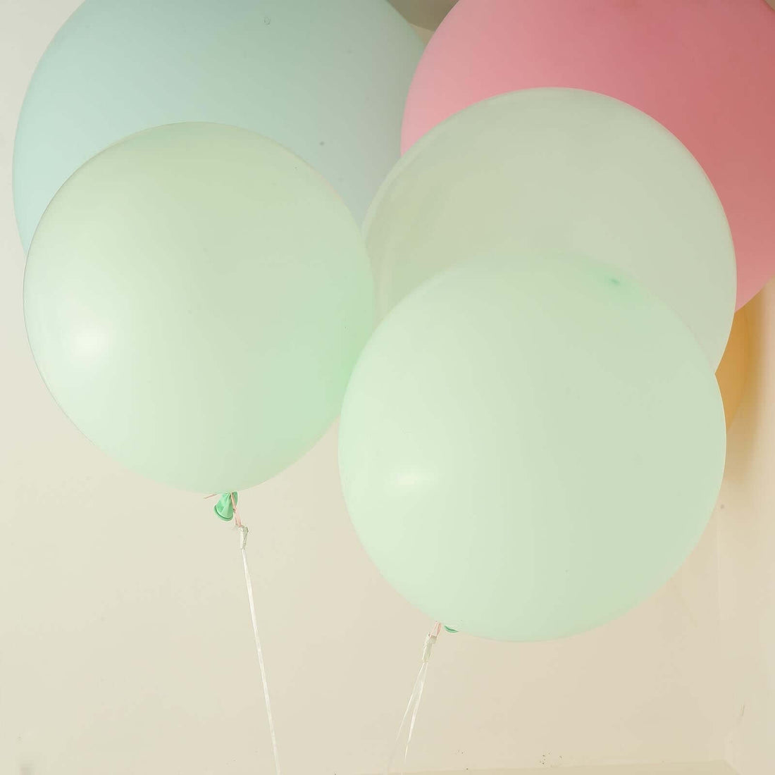 Pastel balloons in green and pink hues against a plain background