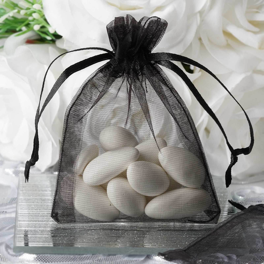 Black organza bag filled with white candies on a reflective surface.