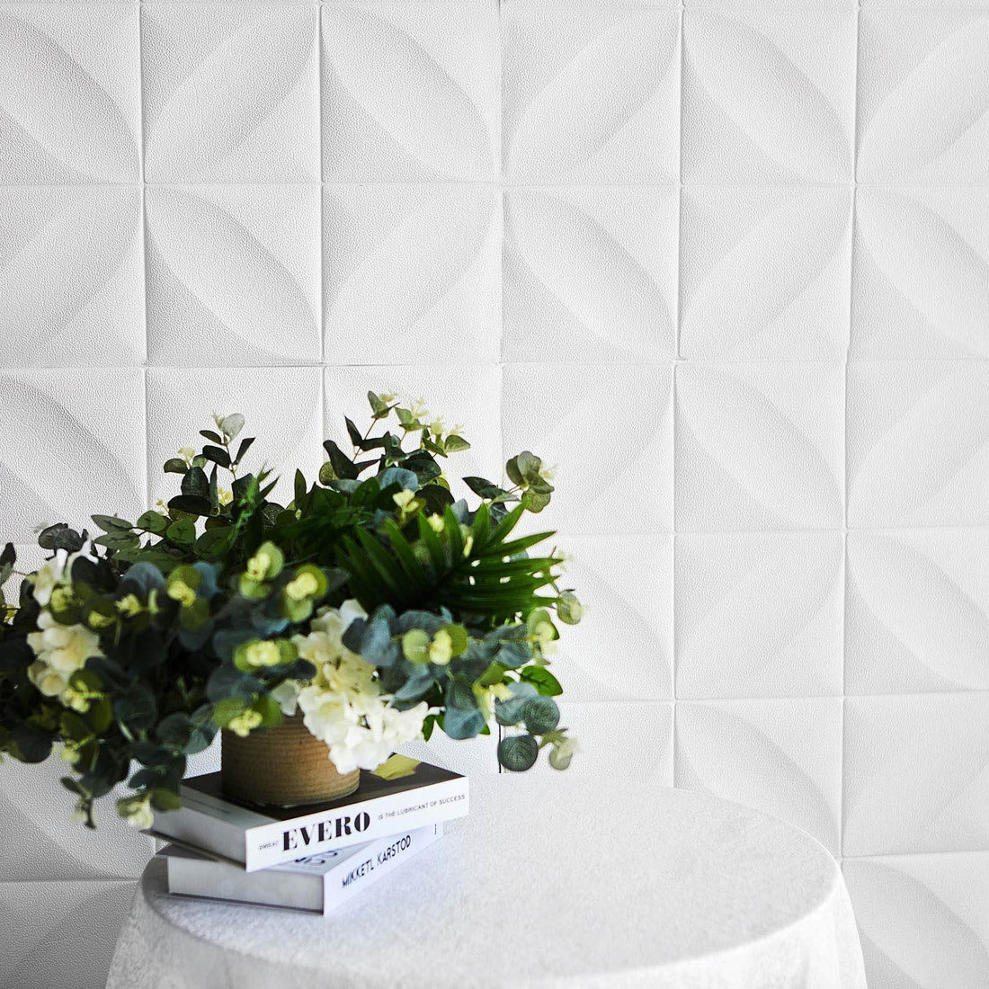 Decorative plant arrangement on a table with textured white wall backdrop.